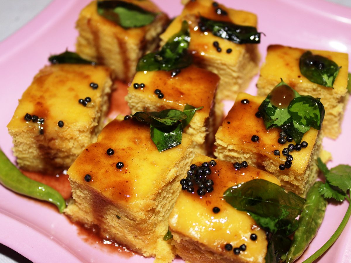 Steamed khaman, a soft yellow Gujarati chickpea flour cake, garnished with mustard seeds and coriander